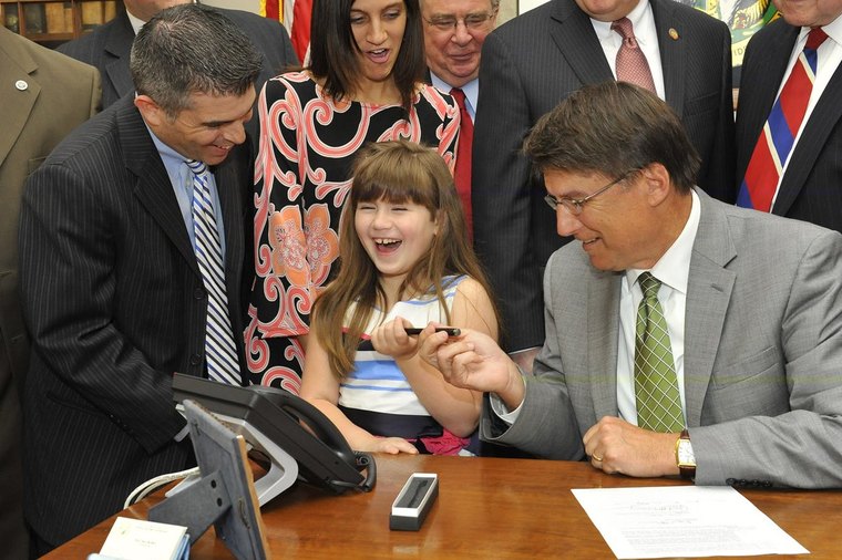 Governor Pat McCrory hands Grace Sanchez the signing pen for North Carolina Senate Bill 98, with Eric Sanchez standing beside her